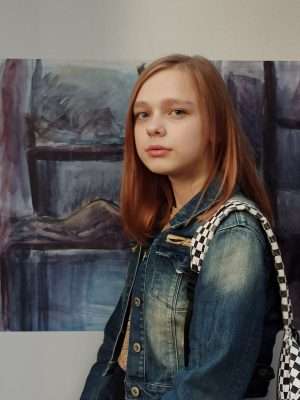 A girl in a jean jacket stands in front of a painting.