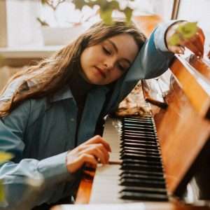 A student leans plays a few notes while leaning on a piano.