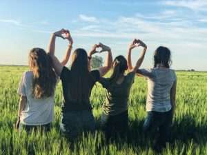 A group of girls standing in a field with their backs to the camera, making the shape of hearts with their hands